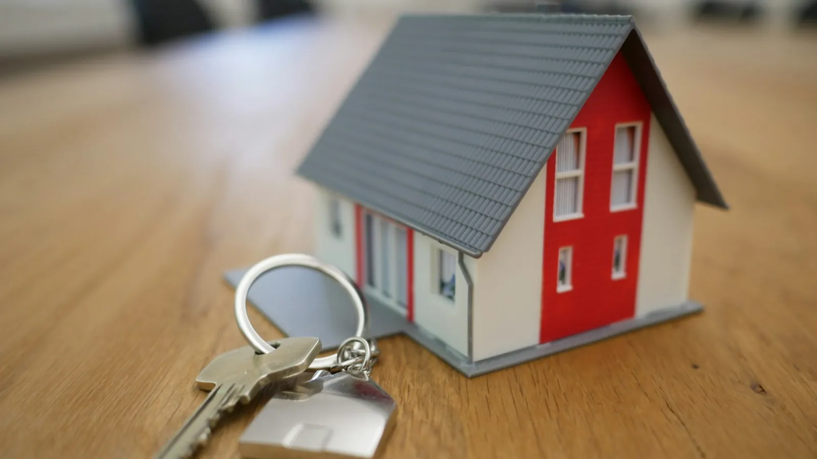 Miniatura de casa e chaves sobre mesa de madeira